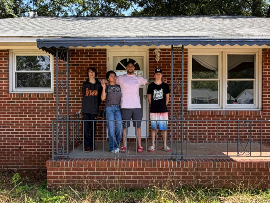 Eli with his wife and two sons on the porch of the first Do Well Housing home